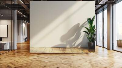 Minimalist room with a wooden floor, a dark gray upholstered chair to the right, and a potted plant with long green leaves beside it, set against a plain white wall illuminated by natural light Wall mural