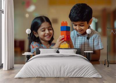 Two Asian Indian children, a girl and a boy, happily playing together while building a tower with colorful blocks in a well-lit room Wall mural