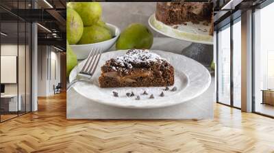 Side view of chocolate pear cake with fork, chocolate chips, and powdered sugar.  Pears and full cake in background. Wall mural