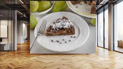 Top side view of Chocolate Pear Cake on a white plate sprinkled with powdered sugar and chocolate chips.  Pears and full cake in background. Wall mural