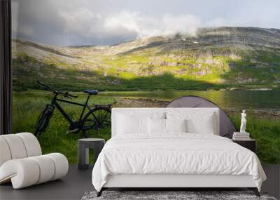 Bike with trekking tent next to a fjord in Norway with mountains and mist in the background Wall mural