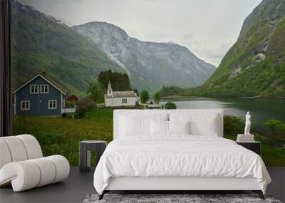 traditional old fashioned white wooden stave church in the beautiful and tranquil landscape at the Naeroyfjord in Norway with snow covered mountains in the background. Wall mural