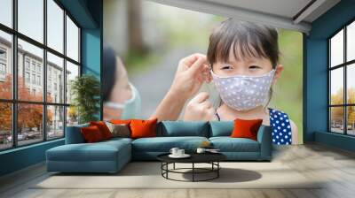 Mother is wearing a cloth mask for little girl protect herself from Coronavirus when child leave the house mom is wearing mask on her nose for safety outdoor activity,illness or Air pollution Wall mural