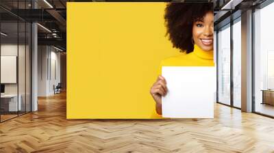 happy woman looking at a camera holding a white sign on a yellow background - copy space mockup Wall mural