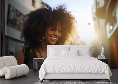 Latin girl with unruly hair smiling and walking through the city with a mobile phone in her hand Wall mural