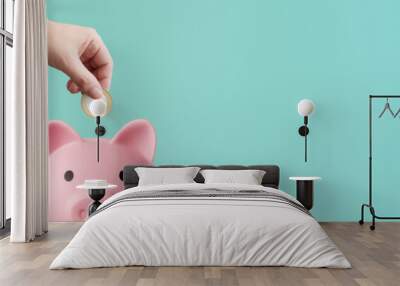 man depositing coins in a pink piggy bank on a blue background - savings concept Wall mural