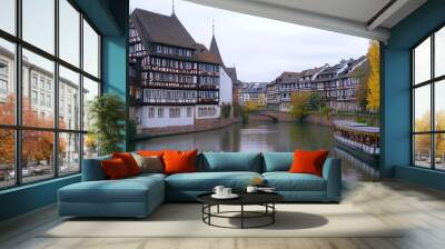 A tranquil scene captures traditional half-timbered houses lining a serene canal, creating a picturesque setting. The buildings, showcasing charming and vibrant architecture with colorful window shutt Wall mural