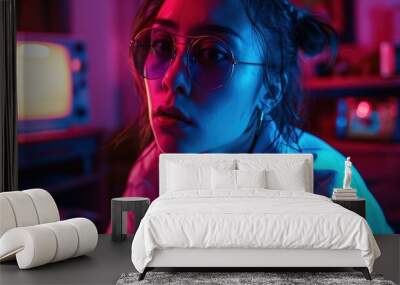 A young woman with glasses is photographed in a room with colorful lighting. The lighting is predominantly blue and pink, casting a vibrant glow on her face. She is gazing off to the side with a thoug Wall mural