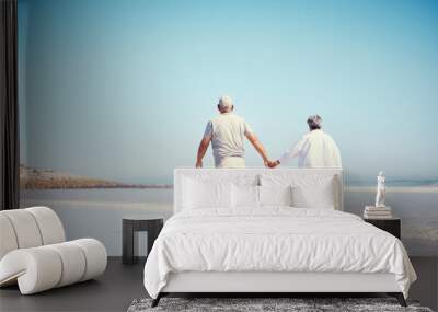 Holding hands, beach and an old couple walking outdoor in summer with blue sky mockup from behind. Love, romance or mock up with a senior man and woman taking a walk on the sand by the ocean or sea Wall mural