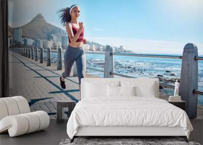 Woman running at ocean promenade for fitness, energy and strong body in Cape Town. Female runner, sports person and athlete at seaside for marathon, cardio exercise and healthy summer workout in sun Wall mural