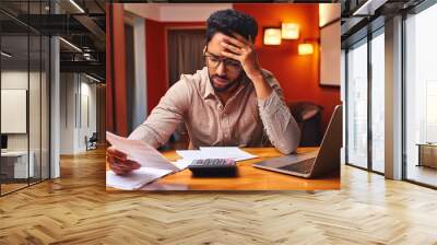 Stressed out concerned man working on laptop reviewing paperwork or bills Wall mural