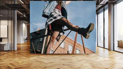 Beautiful grunge (rock) girl takes a step down the stairs. Informal model dressed in jean jacket, checkered shirt, boots and holey tights. Grungy texture effect Wall mural