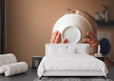 blond kid boy, very hungry eats and holds a plate with both hands, close-up with copyspace Wall mural