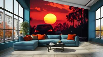  A car traverses a street as the sun sinks behind it, framed by trees along the roadside Wall mural