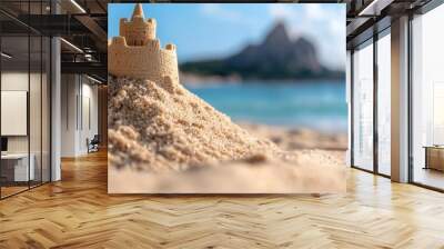  A sandcastle atop a sandy beach, beside a body of water, and a mountain in the backdrop Wall mural