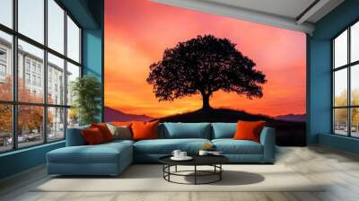  A solitary tree atop a hill against a red-blue sky, dotted with distant clouds and mountain ranges Wall mural