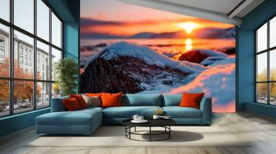  The sun sets over the ocean, its orb sinking below the horizon Snow covers the ground, and nearer, rocks jut out as a rugged foreground Mountains loom in Wall mural