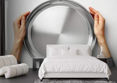   Two hands hold a metal pan against a pristine white backdrop Reflected in the pan's bottom, a clear image of one hand appears Wall mural