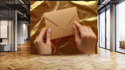 A person holds a sealed envelope over shiny gold wrapping paper on Christmas Day Wall mural