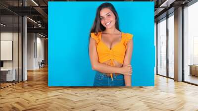 beautiful brunette woman wearing orange tank top over blue background laughing. Wall mural