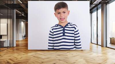 Body language. Disgusted stressed out little cute boy kid wearing stripped t-shirt against white wall, frowning face, demonstrating aversion to something. Wall mural