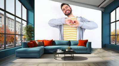 caucasian man wearing casual sportswear over white wall smiling in love doing heart symbol shape with hands. Romantic concept. Wall mural