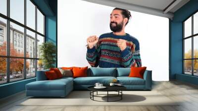 Caucasian man with beard wearing sweater over white background clenches fists and awaits for something nice happened looks away bites lips and waits announcement of results Wall mural