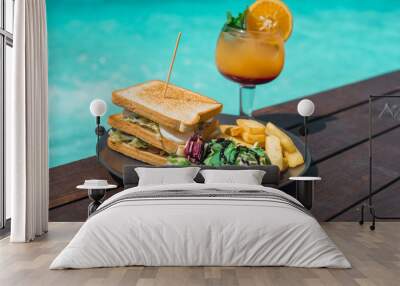 Delicious sandwich  with fries and salad served with cold cocktail next to the pool. Wall mural