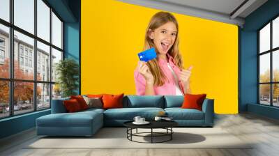 Excited happy positive cheerful smiling Beautiful caucasian kid girl wearing pink shirt hold credit card raise fist in victory Wall mural