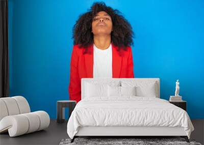 Gloomy, bored young businesswoman with afro hairstyle wearing red over blue background frowns face looking up, being upset with so much talking hands down, feels tired and wants to leave. Wall mural