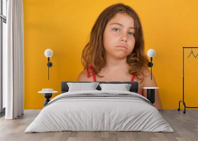 Gloomy, bored young Caucasian girl standing against yellow background frowns face looking up, being upset with so much talking hands down, feels tired and wants to leave. Wall mural