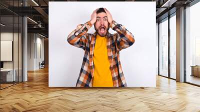 Horrible, stress, shock. Portrait emotional crazy young caucasian man wearing plaid shirt over white background clasping head in hands. Emotions, facial expression concept. Wall mural