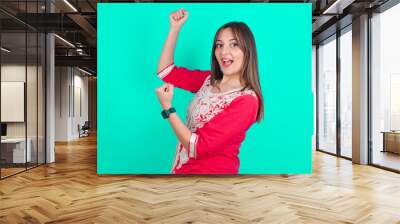 Profile photo of excited young beautiful moroccan woman wearing traditional caftan dress over green background raising fists celebrating black Friday shopping Wall mural