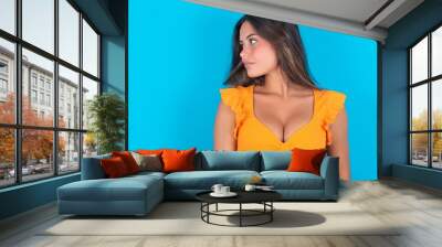 Side view of young happy smiling beautiful brunette woman wearing orange tank top over blue background  Wall mural