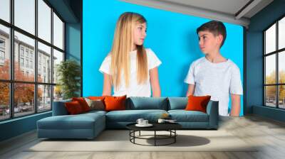 Side view of young happy smiling two kids boy and girl standing over blue studio background Wall mural