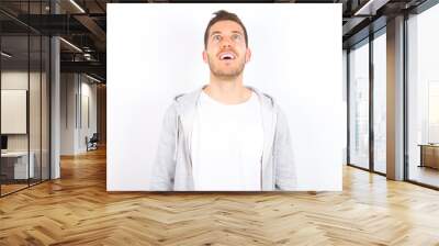 Surprised young caucasian man wearing casual clothes over white background, shrugs shoulders, looking sideways, being happy and excited. Sudden reactions concept. Wall mural