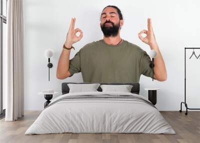 young bearded hispanic man wearing green t-shirt over white background relax and smiling with eyes closed doing meditation gesture with fingers. Yoga concept. Wall mural