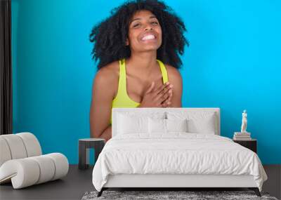 young woman with afro hairstyle in sportswear against blue background, feeling happy, smiling and clapping hands, saying congratulations with an applause. Wall mural