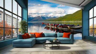 Red boats lined up on a dock reflected in a beautiful lake with snow-capped mountains in the background at Lake McDonald in Glacier National Park Wall mural