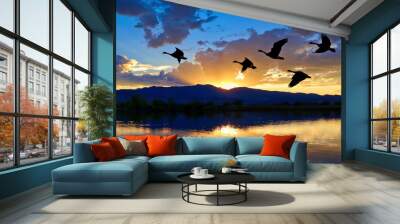 Canada geese flying over a lake at sunset Wall mural