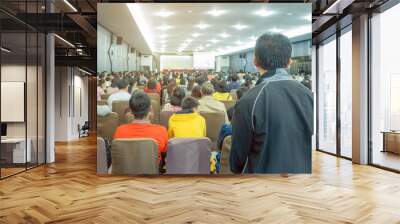 Backside view of spectators standing in a gathering in the back of auditorium full of people. Selective focus. Wall mural