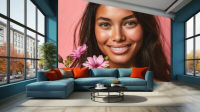 Close-up portrait of a beautiful young woman smiling and holding flowers isolated over pink background Wall mural