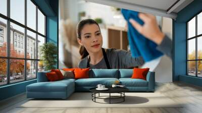 A focused young woman wipes a mirror clean, engaging in household chores to maintain a tidy and sparkling home environment. Wall mural