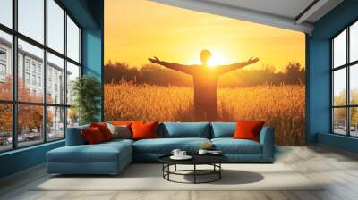 A serene silhouette of a person standing in a field, arms outstretched towards a beautiful sunset, symbolizing freedom and joy. Wall mural