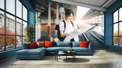 summer, relax, vacation, travel, portrait of a cute Asian girl looking at a map to plan a trip while waiting at the train station. Wall mural