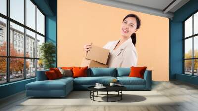 portrait of happy successful confident young asian business woman wearing white jacket holding parcel box isolated on beige studio background, Delivery courier and shipping service concept. Wall mural