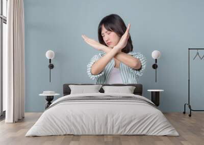 serious asian woman shows cross hands gesture, stop sign, taboo, disapproves bad action, stands in white and green shirt over pastel green background Wall mural