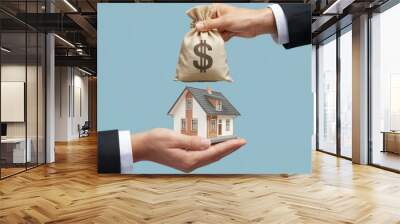 A hand holding a money bag over a miniature house, symbolizing investment. Wall mural