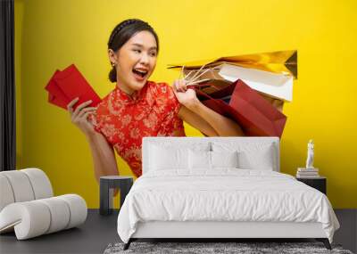 Beautiful Asian woman wearing traditional cheongsam holding red envelope and shopping bag isolated on yellow background, Happy Chinese New Year. Wall mural