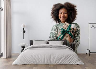 Portrait of young attractive african american woman with curly hair hugging gift box in studio on white background. Wall mural